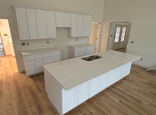 kitchen featuring a center island with sink, white cabinets, a towering ceiling, light wood-style flooring, and a sink