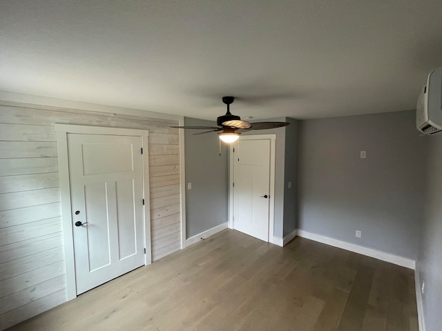 empty room with wood walls, a wall unit AC, wood-type flooring, and ceiling fan