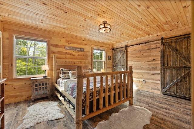 bedroom with a barn door, wooden walls, and wood-type flooring