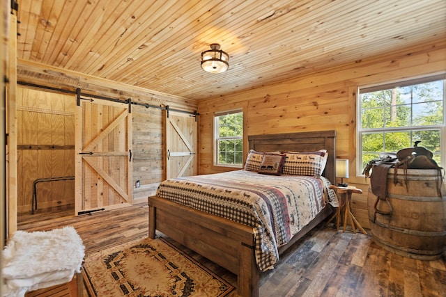 bedroom with a barn door, wooden ceiling, wood walls, and hardwood / wood-style floors