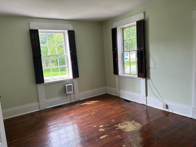 spare room featuring a healthy amount of sunlight, dark hardwood / wood-style flooring, and an AC wall unit