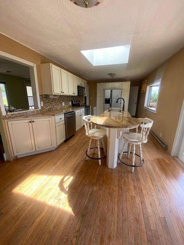 kitchen with light hardwood / wood-style floors, a baseboard heating unit, stainless steel appliances, and a skylight