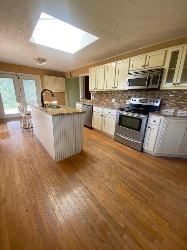 kitchen featuring sink, a skylight, appliances with stainless steel finishes, and light hardwood / wood-style floors