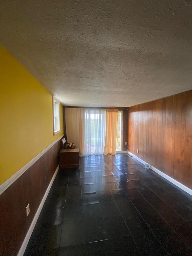 tiled empty room featuring wood walls, a wealth of natural light, and a textured ceiling