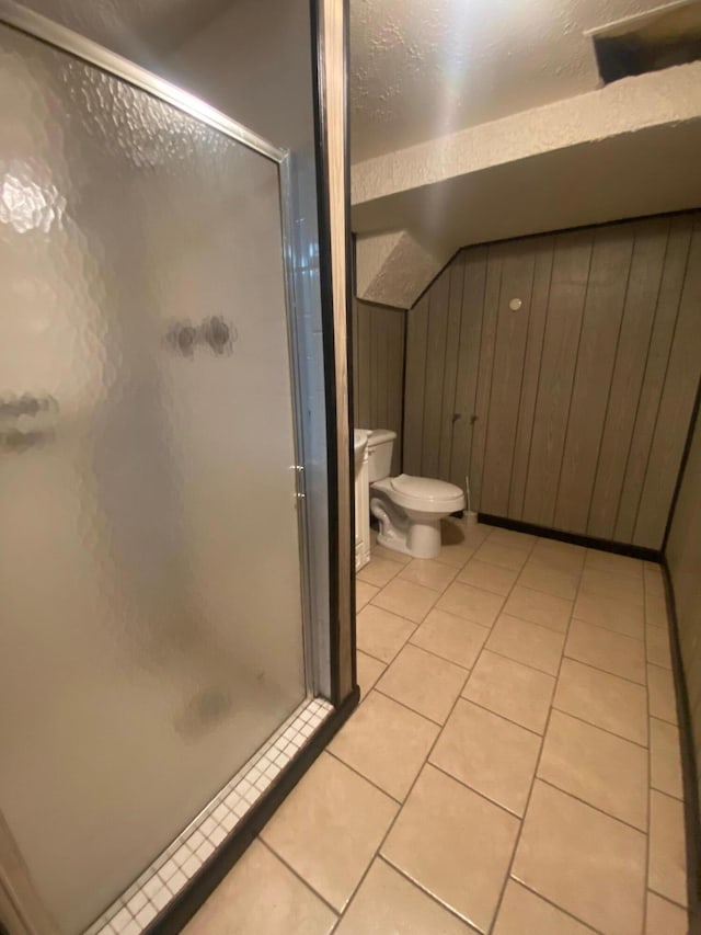 bathroom featuring tile patterned flooring, wooden walls, a shower with door, and toilet