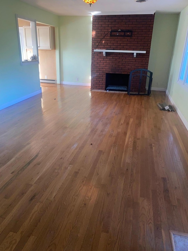 unfurnished living room featuring a fireplace, brick wall, a baseboard radiator, and wood-type flooring