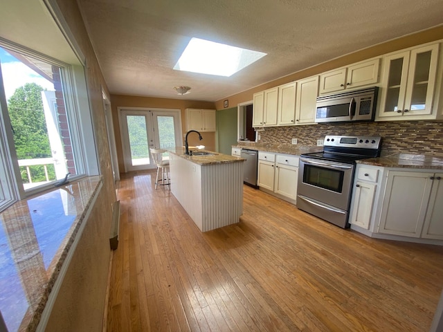 kitchen featuring appliances with stainless steel finishes, light hardwood / wood-style flooring, a center island with sink, and a skylight