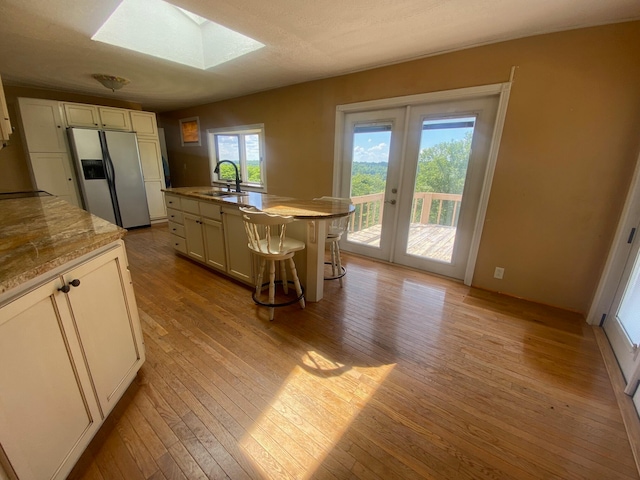 kitchen featuring light hardwood / wood-style flooring, a skylight, stainless steel refrigerator with ice dispenser, plenty of natural light, and a center island with sink