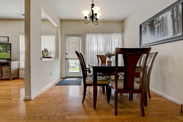 dining space with light wood-type flooring, a textured ceiling, and a chandelier