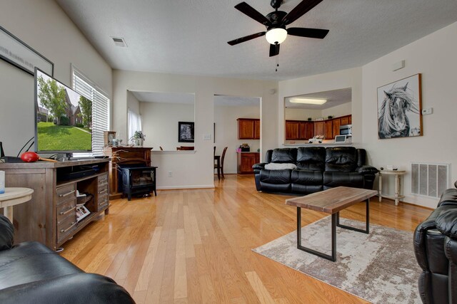 living room with a wood stove, ceiling fan, a textured ceiling, and light hardwood / wood-style floors