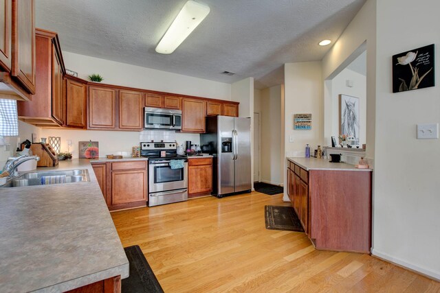 kitchen featuring appliances with stainless steel finishes, a textured ceiling, sink, and light hardwood / wood-style floors