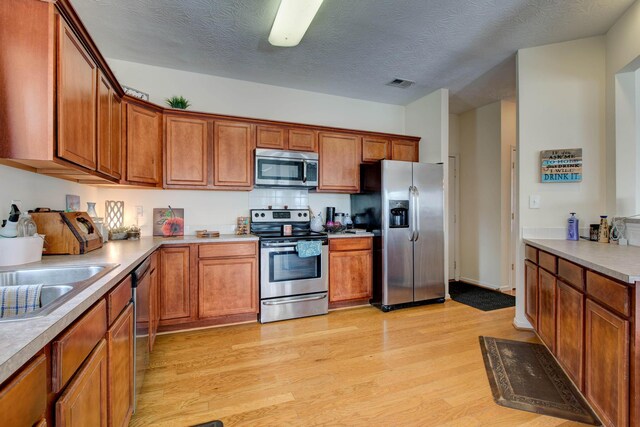 kitchen featuring appliances with stainless steel finishes, sink, a textured ceiling, and light hardwood / wood-style flooring