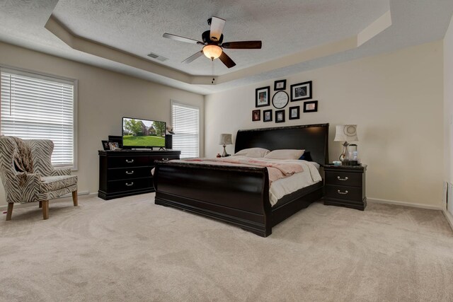 bedroom featuring a tray ceiling, a textured ceiling, ceiling fan, and carpet