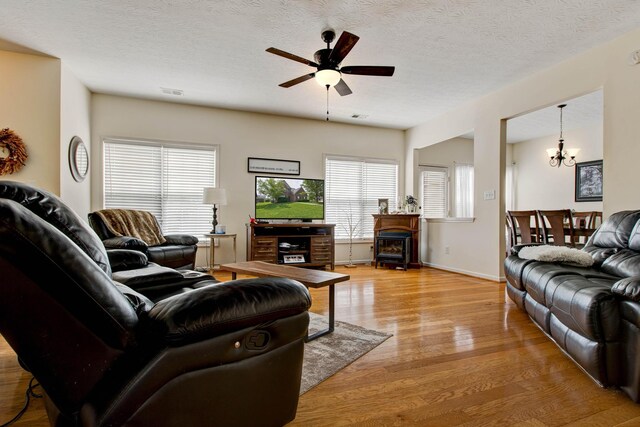 living room featuring a textured ceiling, a healthy amount of sunlight, ceiling fan with notable chandelier, and light hardwood / wood-style flooring