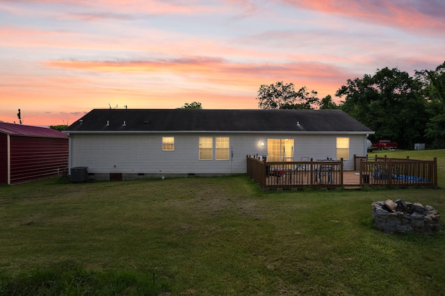 back house at dusk with central air condition unit, an outdoor fire pit, a yard, and a deck