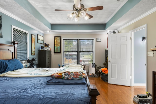 bedroom with a tray ceiling, ornamental molding, ceiling fan, and hardwood / wood-style floors