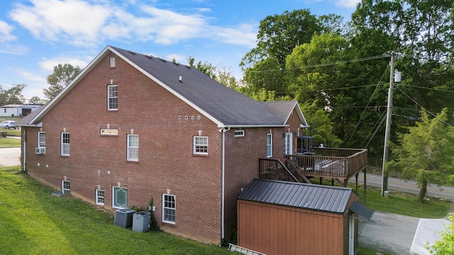 view of property exterior with a yard, a deck, an outdoor structure, and central air condition unit