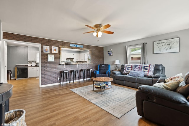 living room with ceiling fan, light hardwood / wood-style floors, and brick wall