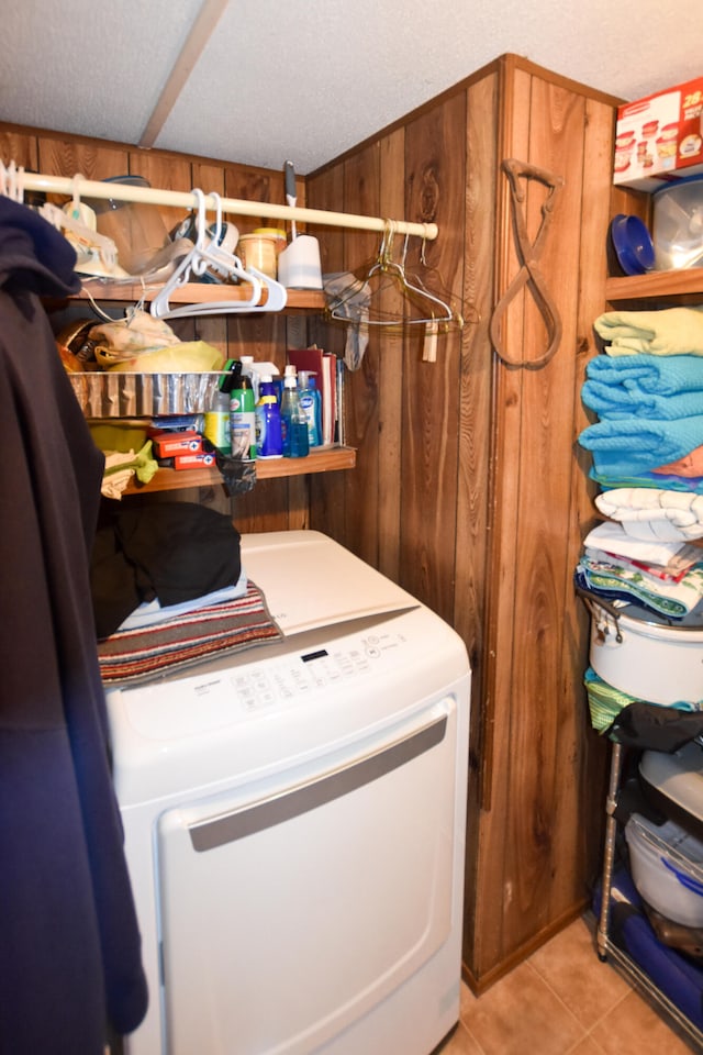 laundry area featuring washer / dryer, wood walls, a textured ceiling, and light tile floors