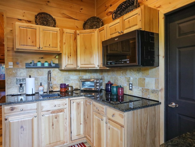 kitchen with dark stone counters, wooden walls, black appliances, and sink