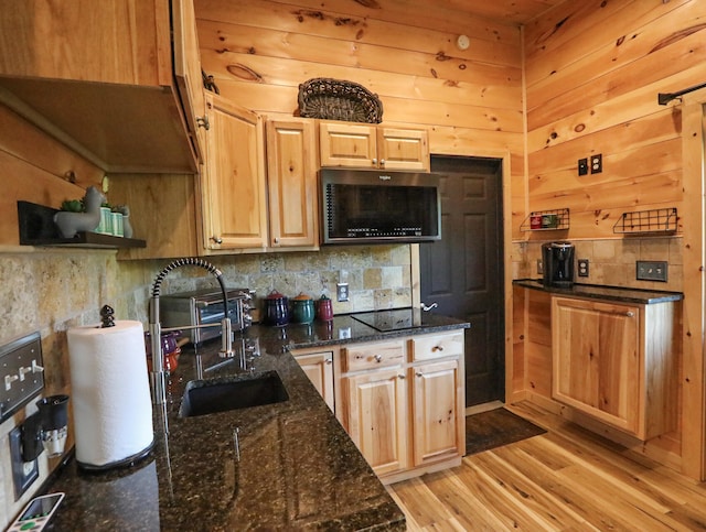 kitchen featuring sink, light hardwood / wood-style flooring, wooden walls, black electric cooktop, and dark stone countertops