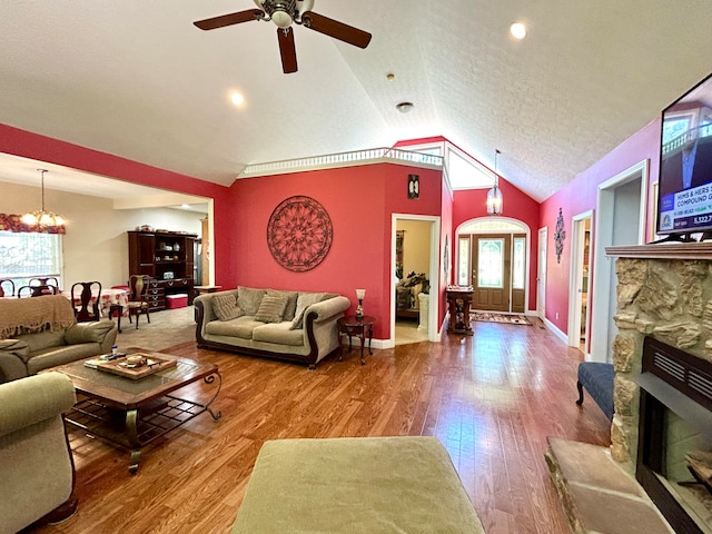 living room featuring a stone fireplace, wood-type flooring, ceiling fan with notable chandelier, a textured ceiling, and high vaulted ceiling