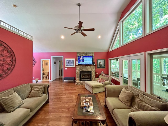 living room with a stone fireplace, ceiling fan, french doors, hardwood / wood-style floors, and high vaulted ceiling