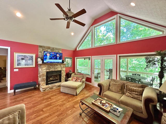 living room with a fireplace, ceiling fan, hardwood / wood-style flooring, high vaulted ceiling, and a textured ceiling