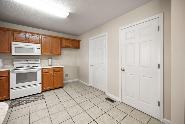 kitchen featuring a textured ceiling, white appliances, and light tile patterned floors