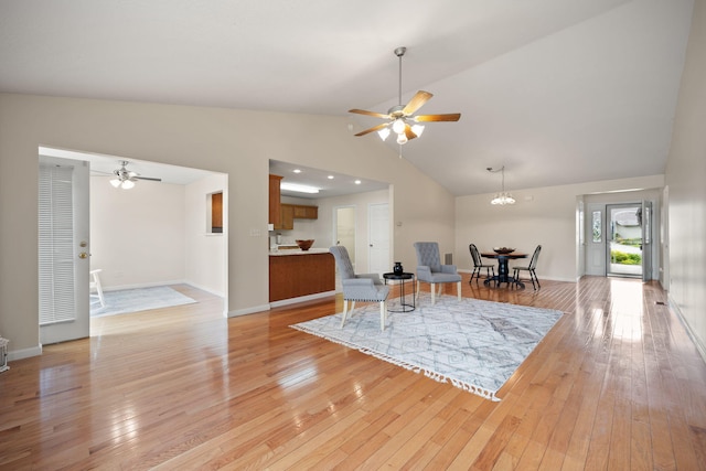 living room with high vaulted ceiling, ceiling fan with notable chandelier, and light hardwood / wood-style floors