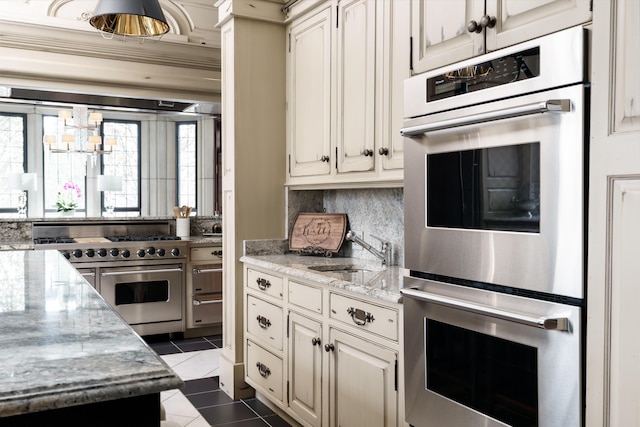 kitchen with dark tile patterned flooring, sink, light stone countertops, tasteful backsplash, and stainless steel appliances