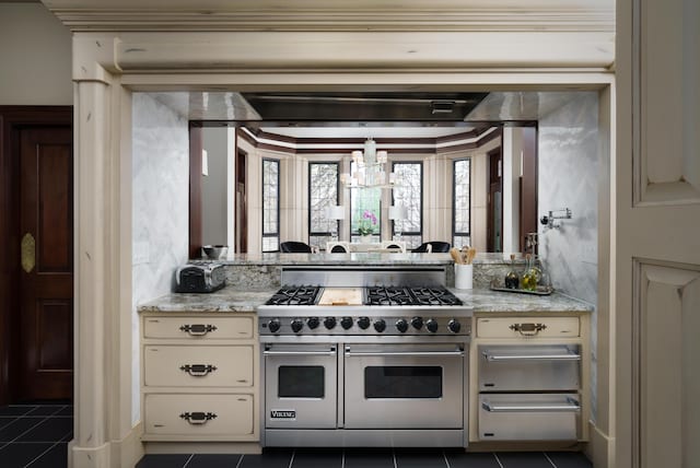 kitchen with cream cabinets, range with two ovens, dark tile patterned floors, and light stone counters