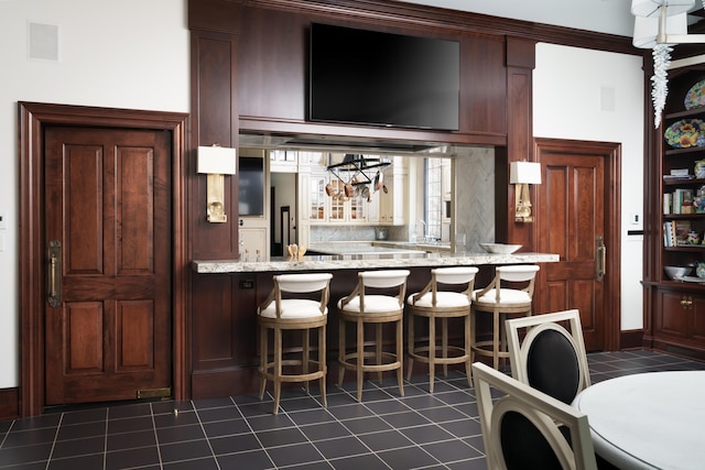 kitchen with a breakfast bar, light stone counters, dark tile patterned floors, and kitchen peninsula