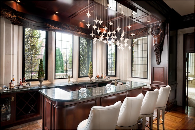 bar with dark stone countertops, plenty of natural light, wood-type flooring, and decorative light fixtures