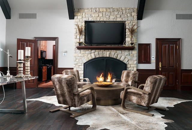 living room featuring beamed ceiling, a stone fireplace, and dark hardwood / wood-style flooring