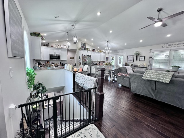 living room with ceiling fan with notable chandelier, dark hardwood / wood-style flooring, and vaulted ceiling