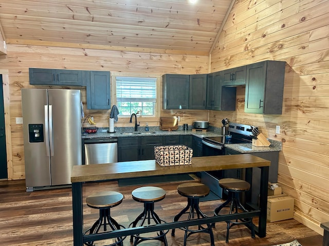 kitchen with wooden walls, dark wood-type flooring, sink, light stone countertops, and appliances with stainless steel finishes