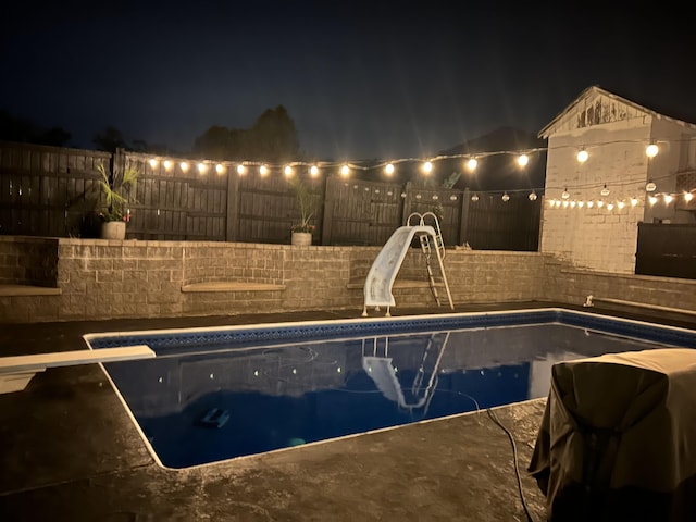 pool at night featuring a diving board and a water slide