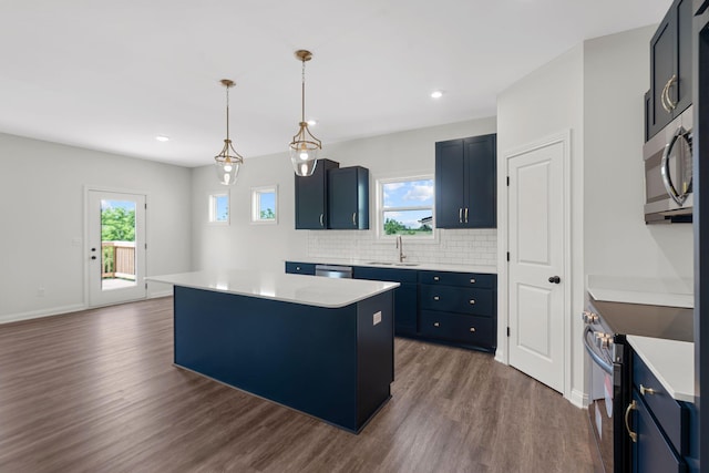 kitchen featuring dark wood-type flooring, hanging light fixtures, a kitchen island, appliances with stainless steel finishes, and sink