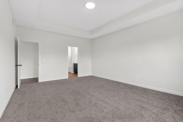 unfurnished bedroom with a raised ceiling and carpet