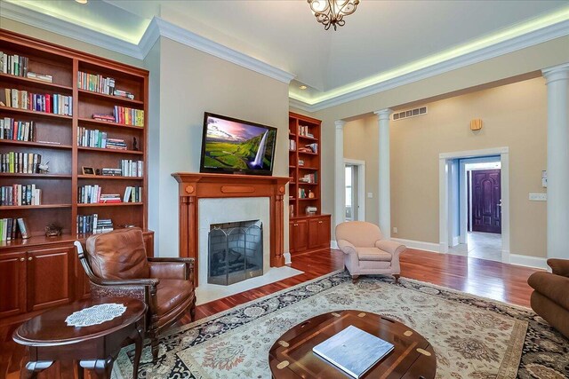 living room with wood-type flooring, built in shelves, ornamental molding, and decorative columns