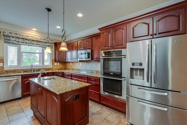 kitchen with light tile flooring, backsplash, a center island with sink, appliances with stainless steel finishes, and pendant lighting