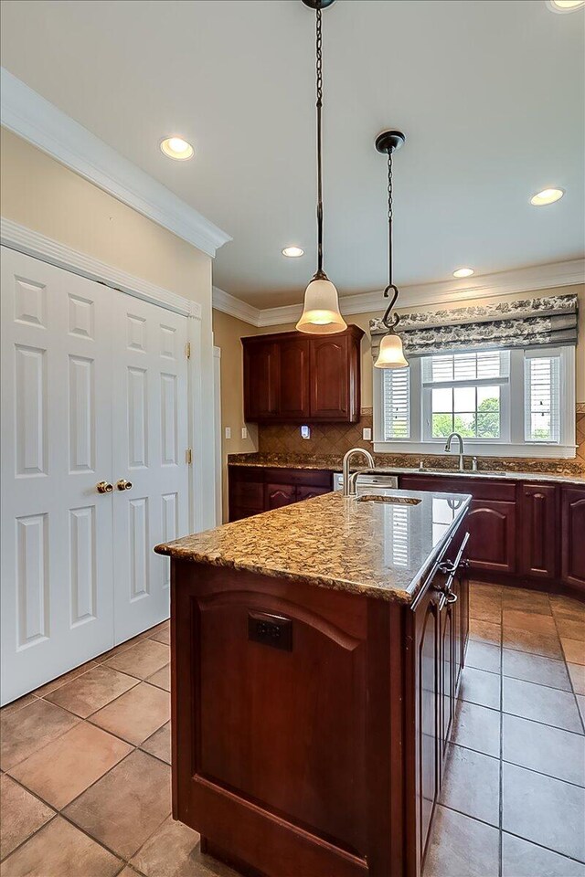 kitchen featuring a center island with sink, light stone counters, tasteful backsplash, and light tile floors