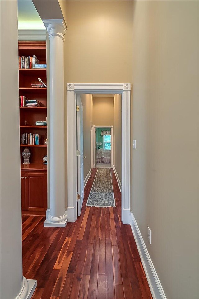 corridor with dark hardwood / wood-style flooring, built in shelves, and decorative columns