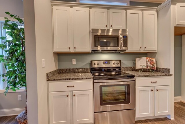 kitchen with dark stone counters, light wood-style flooring, baseboards, and stainless steel appliances