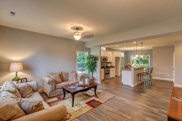 living area with crown molding, dark wood finished floors, visible vents, and baseboards