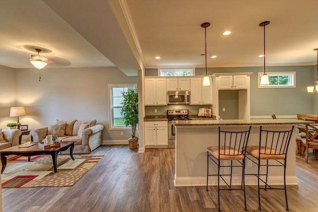 kitchen with pendant lighting, dark hardwood / wood-style floors, a kitchen bar, white cabinetry, and appliances with stainless steel finishes