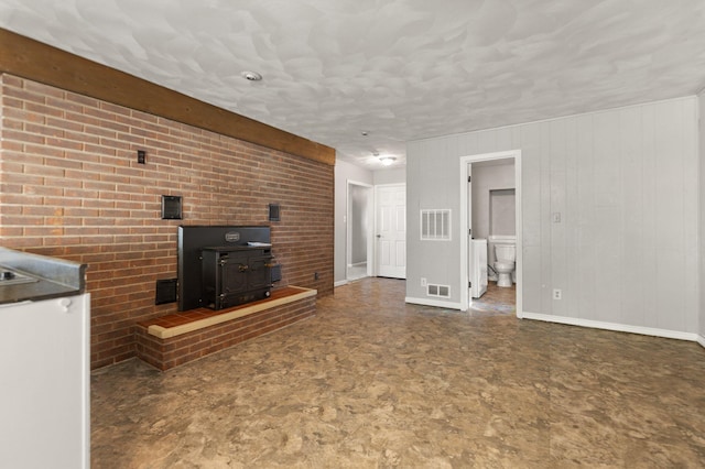 unfurnished living room featuring a wood stove, washer / dryer, and brick wall