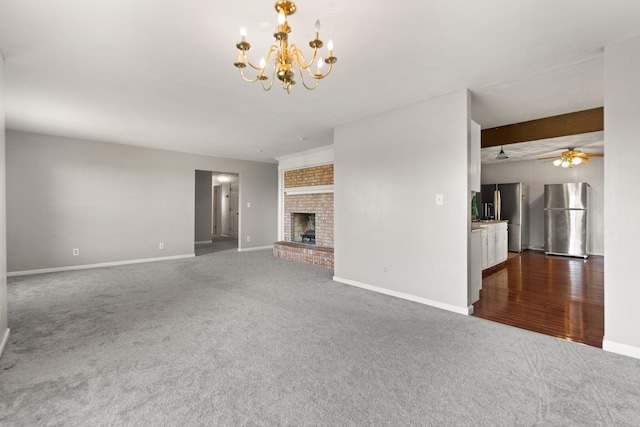 unfurnished living room with ceiling fan with notable chandelier, a brick fireplace, beam ceiling, and dark hardwood / wood-style flooring