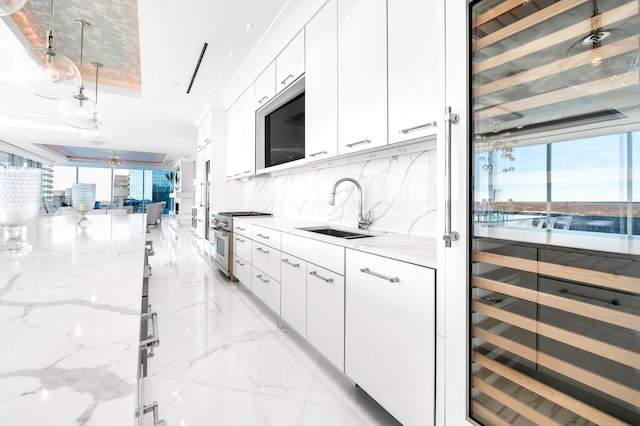 kitchen featuring tasteful backsplash, a raised ceiling, white cabinets, sink, and appliances with stainless steel finishes